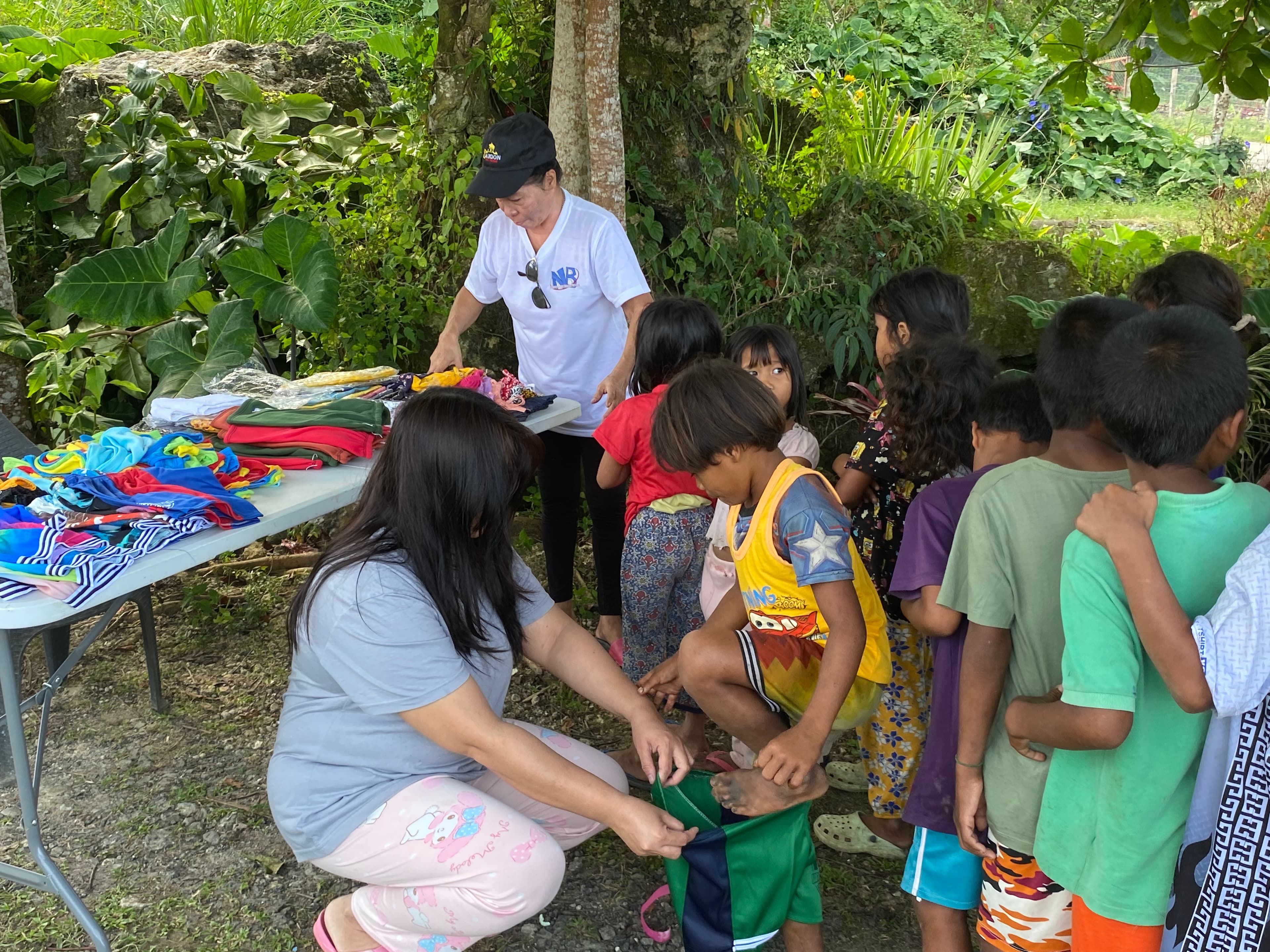 Volunteer kneeling down to help a young child try on a new pair of shorts